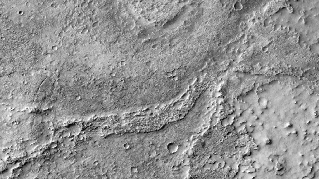 A moderately eroded, sinuous fluvial ridge (FSR) stands out prominently against the surrounding terrain. Its surface is pockmarked by numerous small craters, suggesting prolonged exposure. The ridge emerges from a shallow valley to the northeast and becomes increasingly distinct as it extends westward before gradually fading out. A pronounced curve along its path likely marks an ancient meander. To the north, a circular, flat feature—possibly a former impact crater—appears to have been filled in by water or sediment, smoothing its once-rugged interior.
